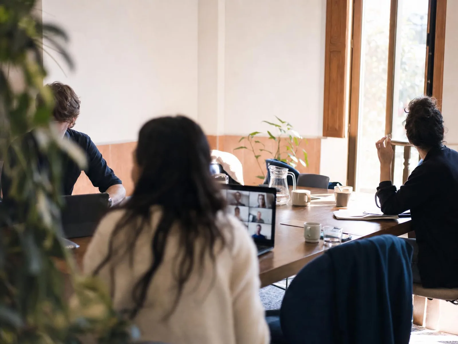 Salle de réunion lumineuse aux murs clairs, chaises tournées dans des directions différentes autour d'une table où traînent des tasses à café et un ordinateur portable ouvert sur un appel vidéo flou.
