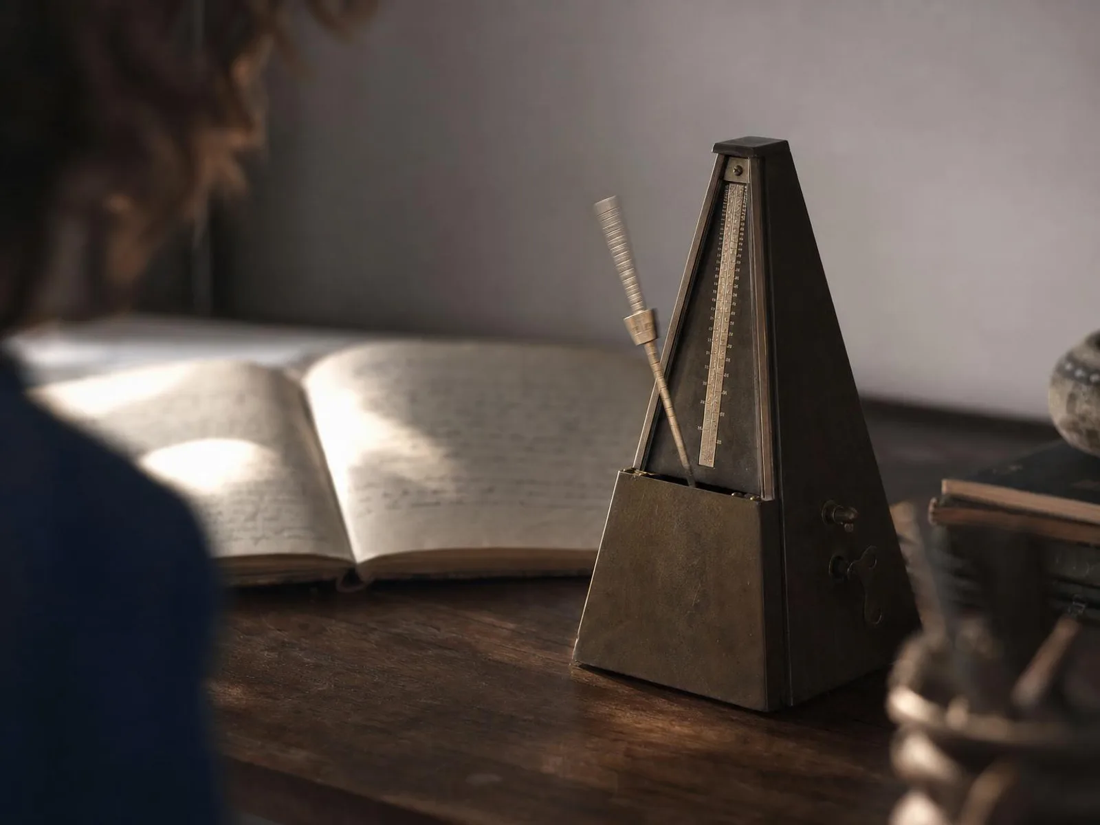 Un métronome en laiton posé sur un bureau en bois sombre, le balancier en mouvement, à côté d'un carnet ouvert flou, dans la lumière chaude d'une lampe de soir.