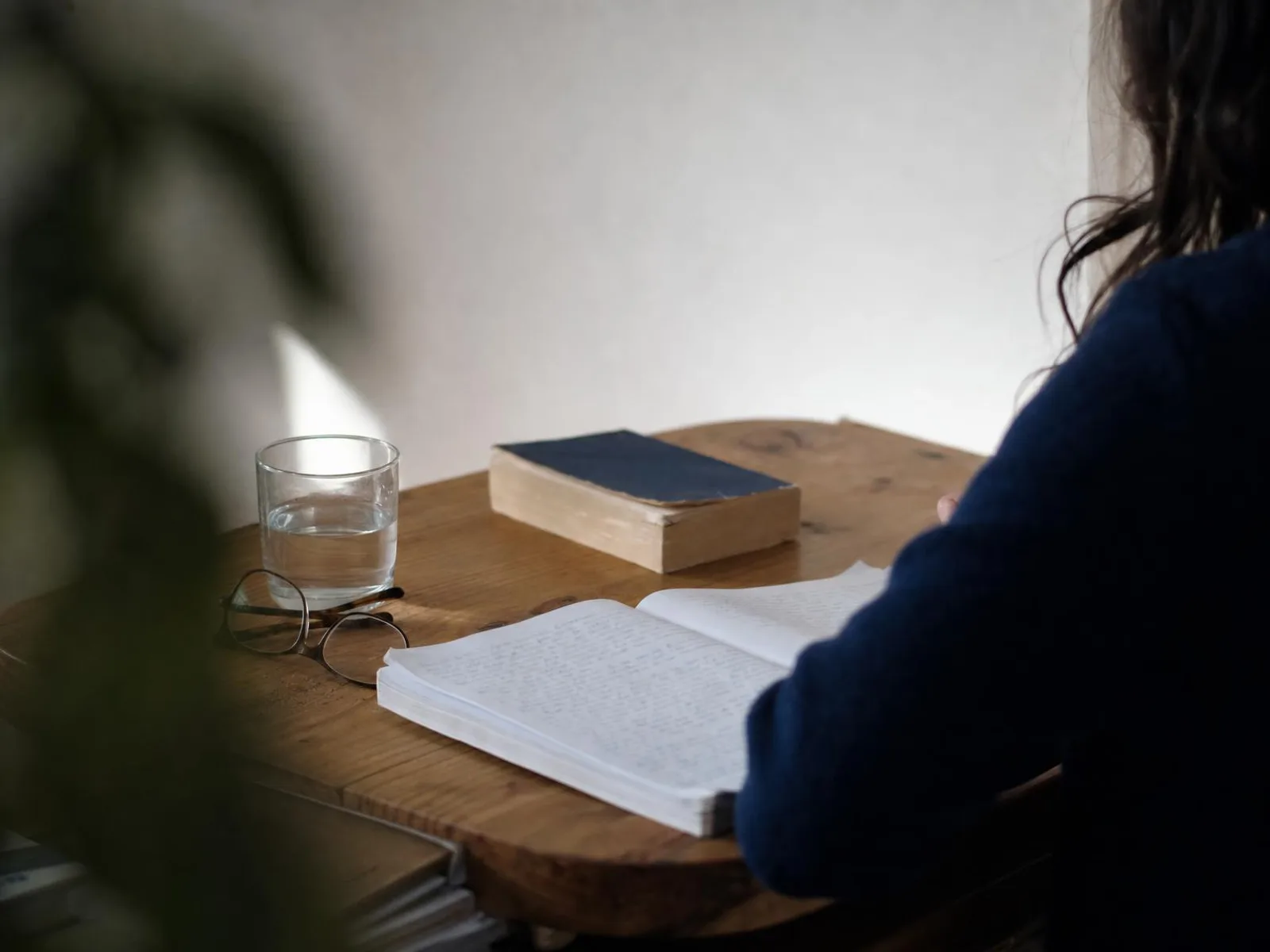 Un bureau éclairé par une lampe le soir, avec un cahier ouvert, un dictionnaire posé à plat, des lunettes et un verre d'eau.