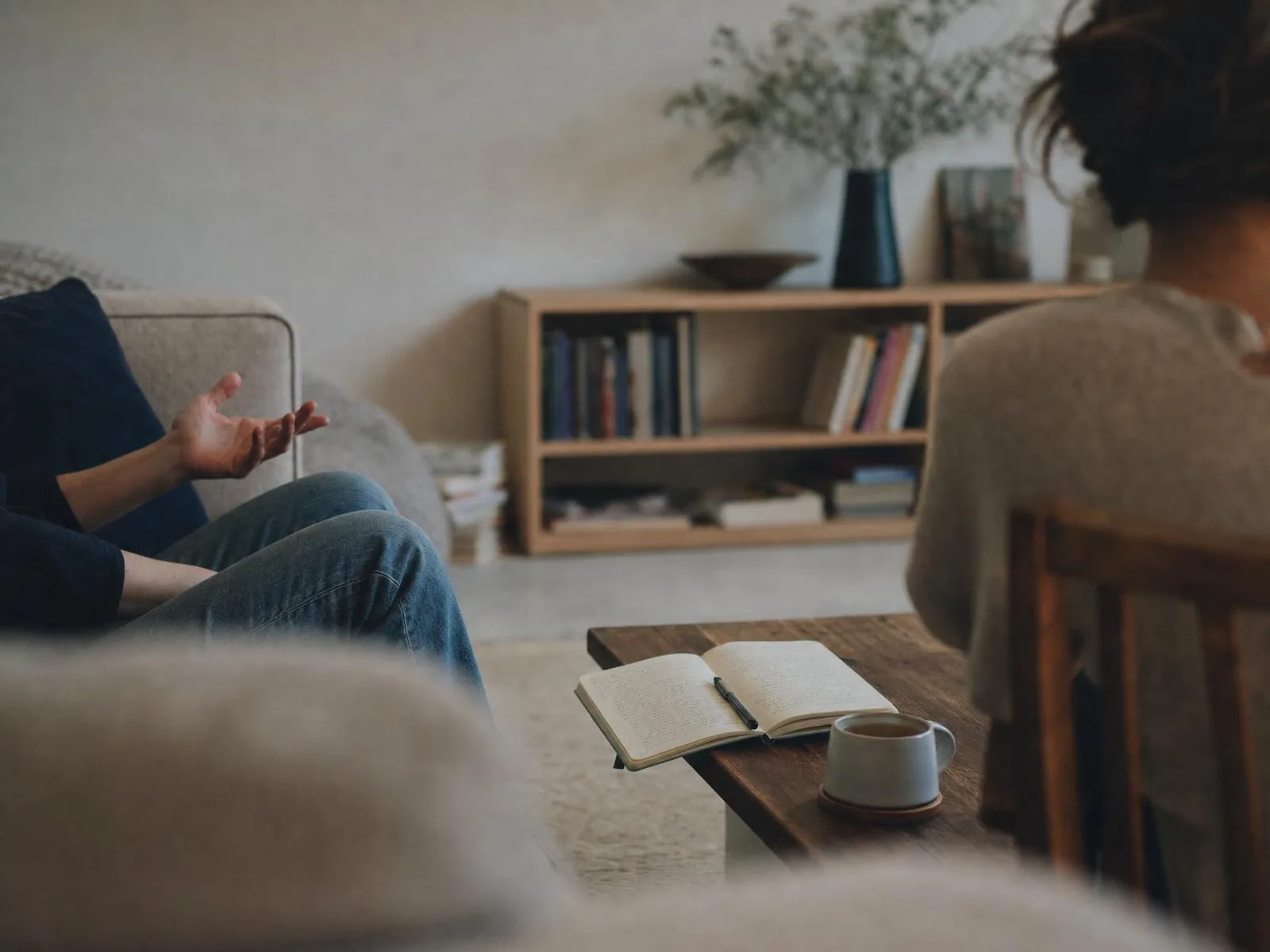 Un carnet ouvert et un stylo posés sur une table basse en bois, à côté d'une tasse, dans la lumière chaude d'une lampe de salon le soir.
