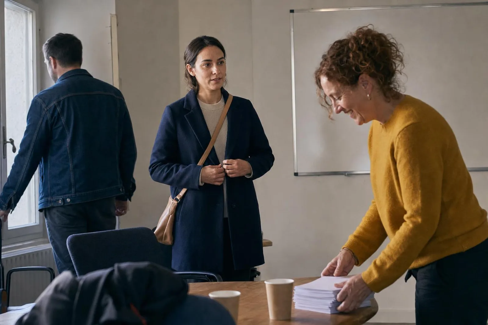 Fin de séance dans une salle de cours : une apprenante reboutonne son manteau en parlant avec sa formatrice, qui rassemble des feuilles sur la table.