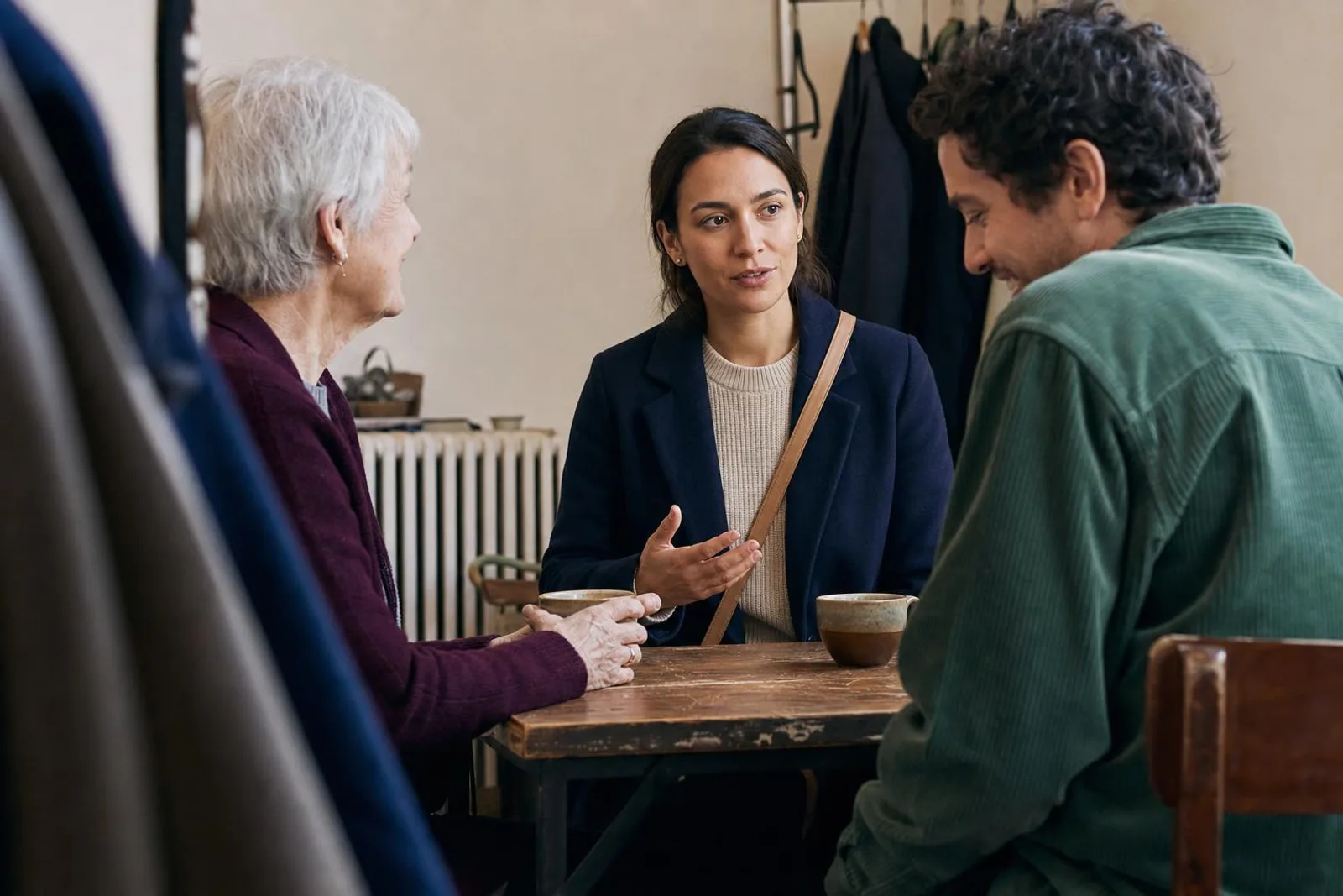À la table d'un café, une cliente parle avec deux personnes autour de tasses vides.