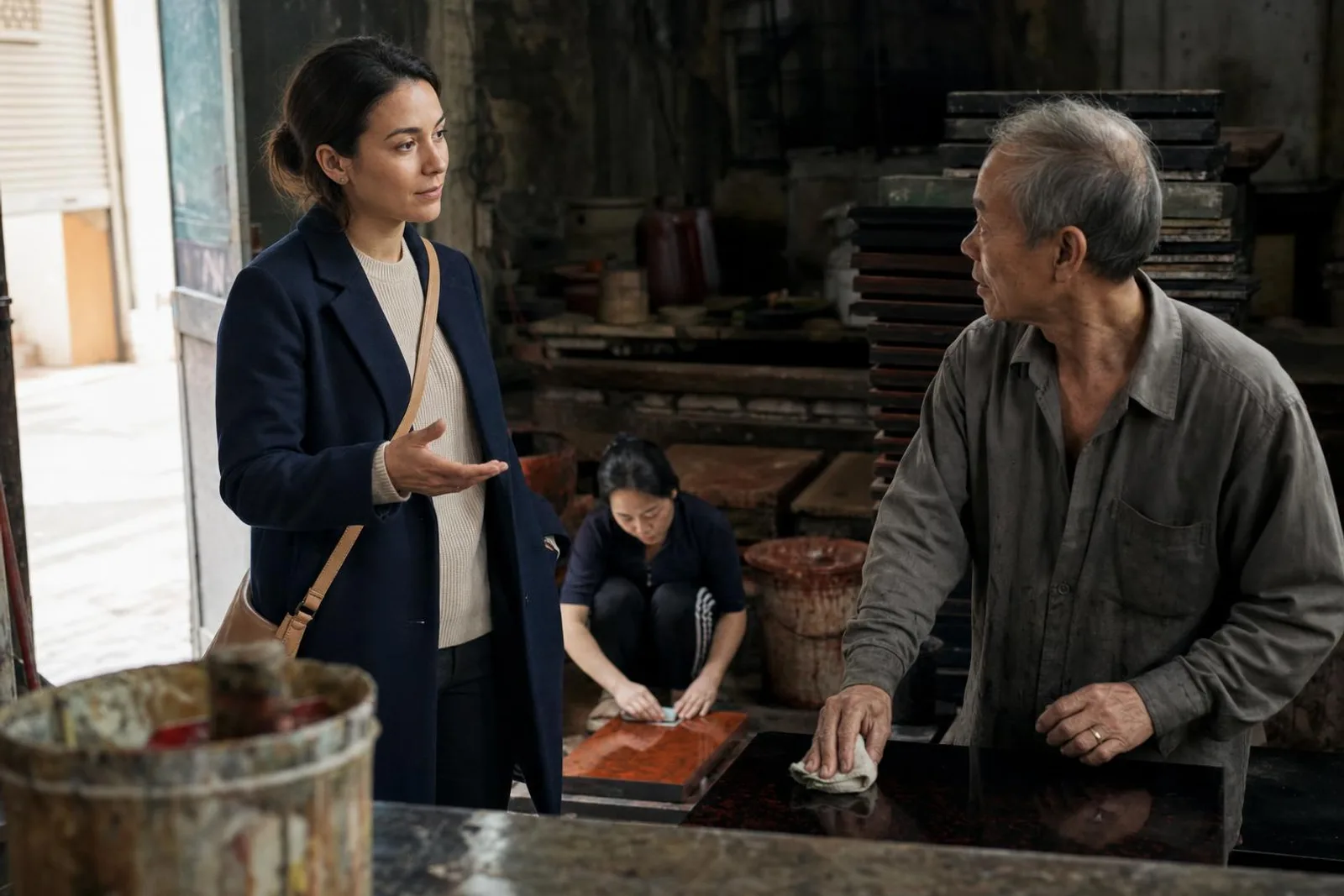 Dans un atelier de laque, une passante converse avec l'artisan qui polit un panneau.